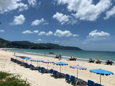 a beach with blue chairs and umbrellas and the ocean at Phuket Condominium Karon beach in Karon Beach