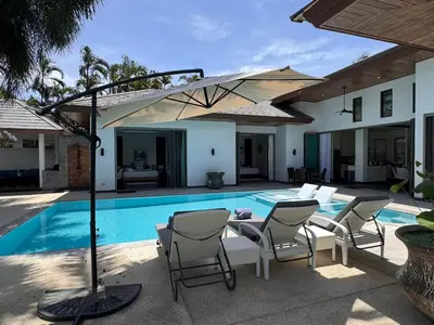 a villa with a swimming pool with chairs and an umbrella at Beautiful villa walking distance from Bangtao Beach in Bang Tao Beach