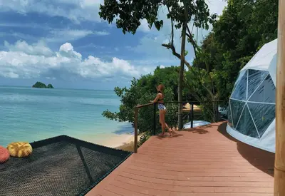 a woman standing on a balcony looking at the ocean at Touch Glamping Koh Yao Noi ทัช แกรมปิ้ง เกาะยาวน้อย in Ko Yao Noi