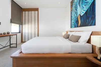 a bedroom with a white bed with a painting on the wall at Eden Escape Naiyang Beach in Phuket Town