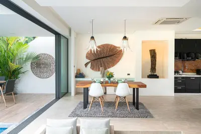 a kitchen and dining room with a wooden table and white chairs at Eden Escape Naiyang Beach in Phuket Town