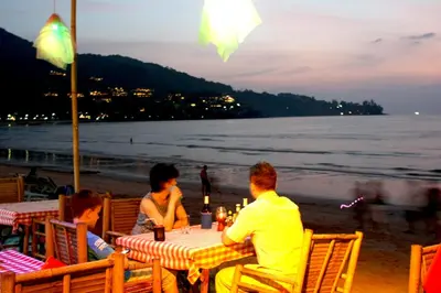 a group of people sitting at a table on the beach at Deng's kamala beach Guesthouse in Kamala Beach