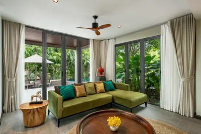 a living room with a green couch and large windows at Noku Phuket in Chalong