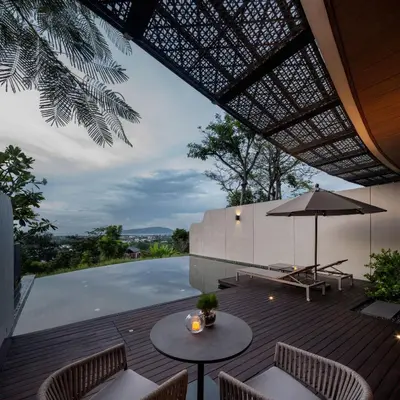 a patio with tables and an umbrella and a pool at Noku Phuket in Chalong