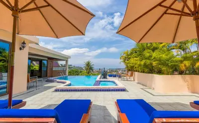 a resort pool with blue chairs and an umbrella at Luxury Four Bed Villa Jasmine, infinity pool, full staff , chef and breakfasts in Kata Beach