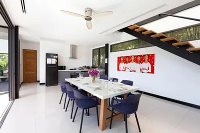 a dining room with a white table and blue chairs at Loft Style 4BR Villa Sunset Garden 4 with 12m Salt Water Pool, near NaiHarn in Rawai Beach
