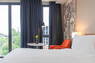a hotel room with a bed and a chair and a window at GLOW Mira Karon Beach in Karon Beach