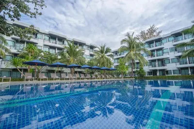 a swimming pool in front of a building with trees and umbrellas at Holiday Style Ao Nang Beach Resort, Krabi in Ao Nang Beach