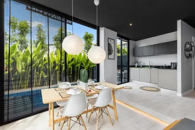 a dining room with a table and chairs and large windows at Villoft Zen Living Resort in Thalang