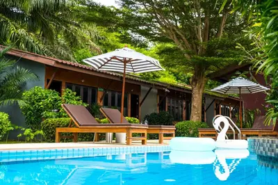 a pool with chairs and umbrellas next to a house at Phuket Siam Villas - SHA PLUS in Chalong