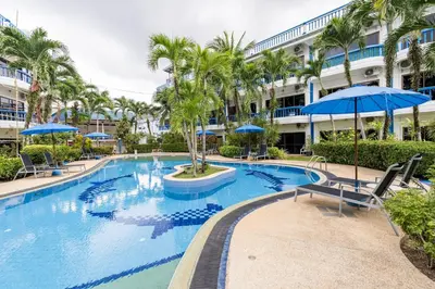 a large swimming pool with palm trees and blue umbrellas at Kamala - The Club Residence -2 BR Pool View Residence in Kamala Beach