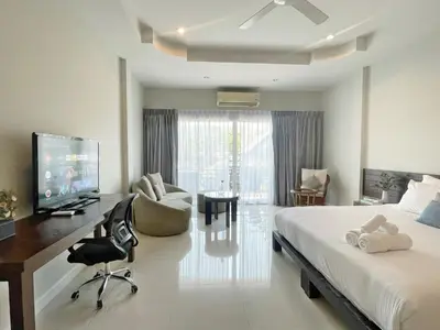 a bedroom with a bed and a desk and a tv at The Langstan Suites in Nai Harn Beach