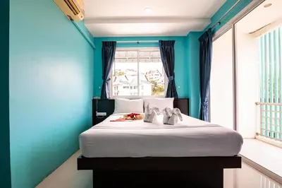 a bedroom with a bed with blue walls and a window at PATONG BLUE HOTEL in Patong Beach
