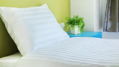 a bed with white sheets and a plant on a table at Kata Bai D - SHA Certificate Hotel in Kata Beach