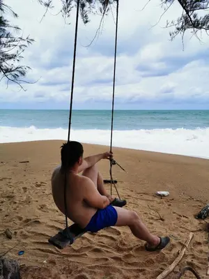 a man sitting on a swing on the beach at Apartments MBC 1308 in Mai Khao Beach