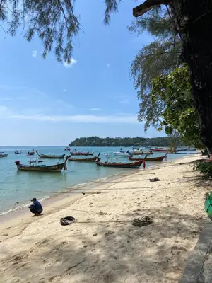 a man sitting on a beach with boats in the water at Title V Mountain View Pool View Gym Hammam in Rawai Beach