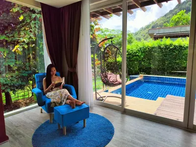a woman sitting in a blue chair reading a book at Phuket Jungle Experience Resort in Karon Beach
