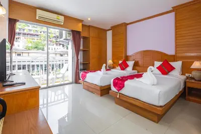 two beds in a room with a desk and a television at Sunshine Patong in Patong Beach