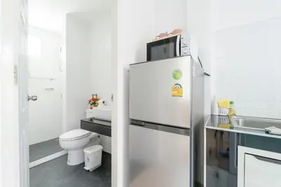 a kitchen with a refrigerator with a microwave on top at White House Apartment - Chalong in Chalong