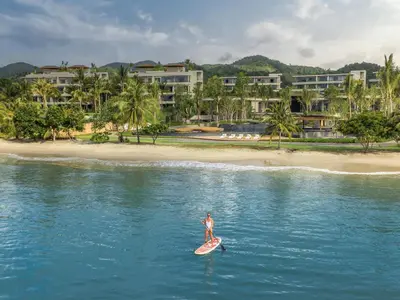a person on a surfboard in the water near a beach at Anantara Koh Yao Yai Resort & Villas in Ko Yao Yai