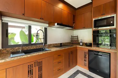 a kitchen with wooden cabinets and a sink and a microwave at Villa Carlos, Luxury 7 BDR Private Pool Villa, Baan Bua Nai Harn, Phuket in Rawai Beach