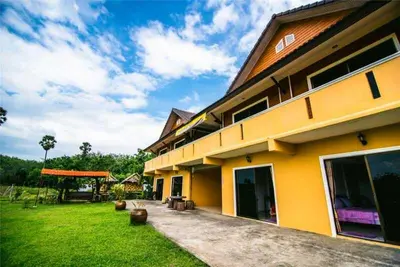 a yellow building with a grass yard next to it at Relaxation guesthouse in Thalang