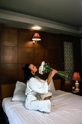 a woman sitting on a bed holding a bouquet of flowers at Grand Orlov Apart Hotel in Patong Beach