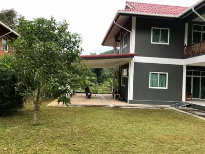 a person sitting on a bench in front of a house at Thanid House in Ban Nai Khlong