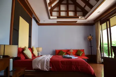 a bedroom with a bed with red sheets and pillows at VILLA SIRINTHARA in Rawai Beach