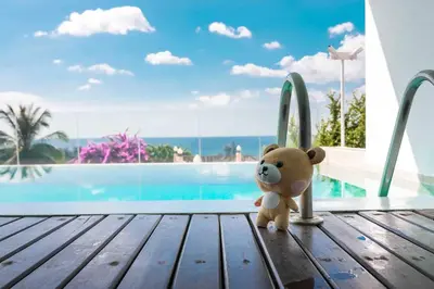 a teddy bear sitting on a wooden deck next to a swimming pool at Large Penthouse 3BR with jacuzzi, Best for Kids in Karon Beach