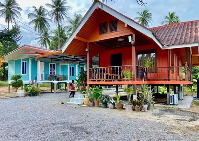 a woman walks past a colorful house with palm trees at Patcharin Homestay in Ban Lo Pla Lai (1)