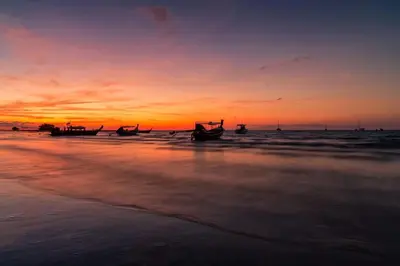 a sunset on the beach with boats in the water at TITLE NaiYang apartment-300m from sea in Phuket Town