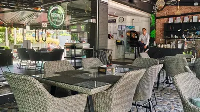 a restaurant with tables and chairs and a man standing in a bar at Lime Hotel in Patong Beach