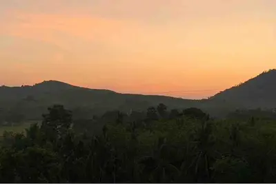 a sunset over a forest with mountains in the background at MaiKhao Sunrise Sight Space in Ban Mai Salae