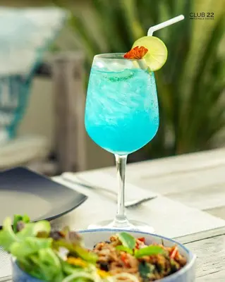 a blue drink in a glass next to a bowl of food at Club22 Kamala Suites, Kamala Beach in Kamala Beach